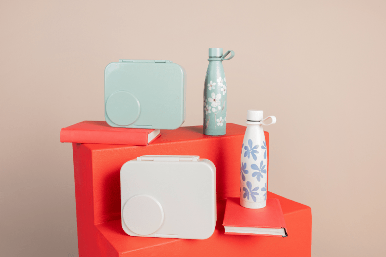 Babyshop pastel bento boxes and reusable water bottles styled on red blocks